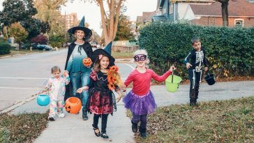 Trick or treat. Mother with children going to trick or treat on Halloween holiday. Mom with kids in party costumes with baskets going to neighbourhood houses for candies, treats.