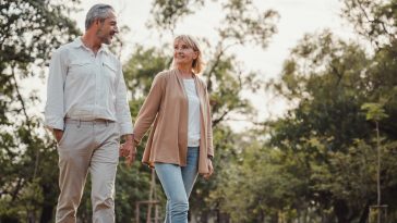 Romantic and elderly healthy lifestyle concept.Senior active caucasian couple holding hands looks happy in the park in the afternoon autumn sunlight,happy anniversary,happily retired with copy space.