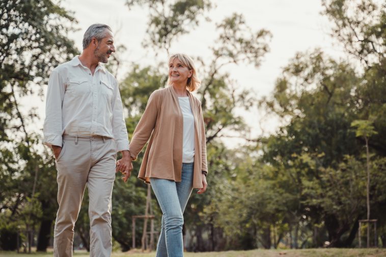 Romantic and elderly healthy lifestyle concept.Senior active caucasian couple holding hands looks happy in the park in the afternoon autumn sunlight,happy anniversary,happily retired with copy space.