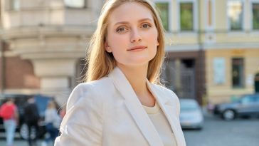 Outdoor portrait of young successful smiling business woman. Beautiful blonde female looking at the camera, city street background