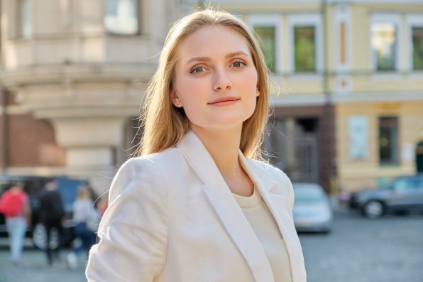 Outdoor portrait of young successful smiling business woman. Beautiful blonde female looking at the camera, city street background