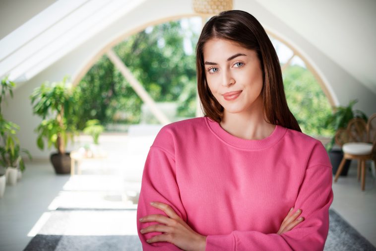 Portrait shot of beautiful young woman standing with arms crossed in the living room.