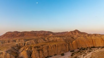 Dawn in the Judean Desert in Israel. A sky with a beautiful gradient, mountains of gold, a dry riverbed and a moon in the sky.