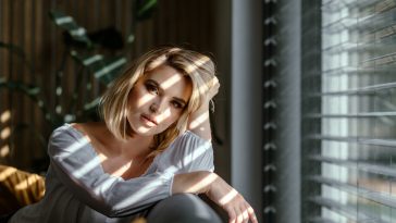 Glamour portrait beautiful lady at home looking through the window with sun beams on face