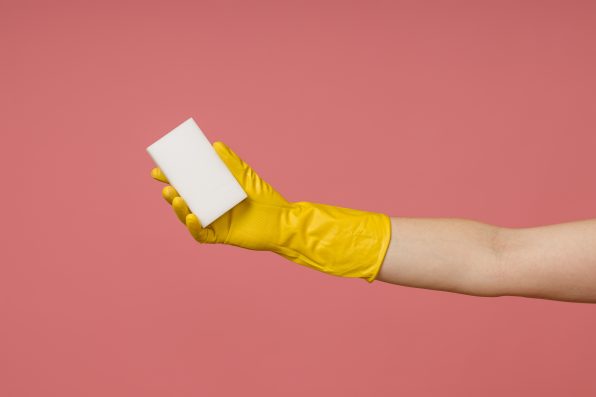 a hand in a rubber glove holds a melamine white sponge