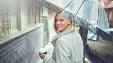 Rearview portrait of an attractive young woman walking in the rain with an umbrella and a coffee.