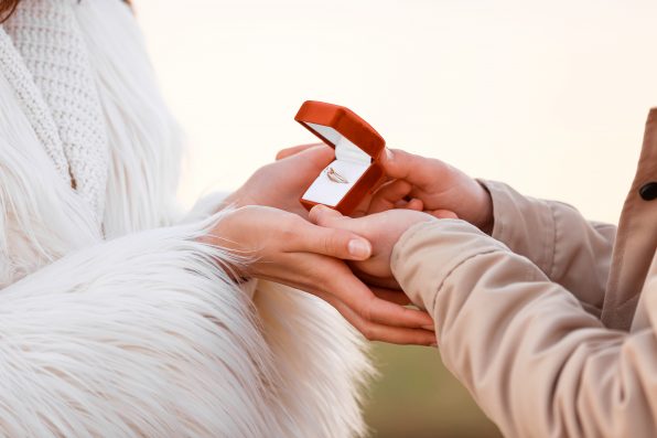 Young couple with engagement ring in box outdoors, closeup