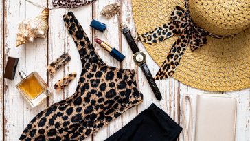 Travel and vacation concept. Flat lay fashion beach holiday accessories with leopard print swimsuit, perfume straw hat, sunglasses and other on wooden background.