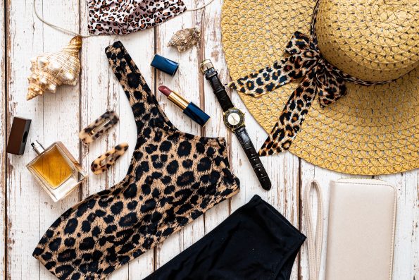 Travel and vacation concept. Flat lay fashion beach holiday accessories with leopard print swimsuit, perfume straw hat, sunglasses and other on wooden background.