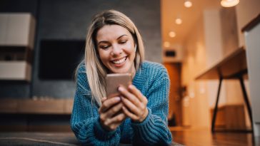 A smiling woman on the floor using phone to hang on social media.