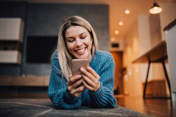 A smiling woman on the floor using phone to hang on social media.