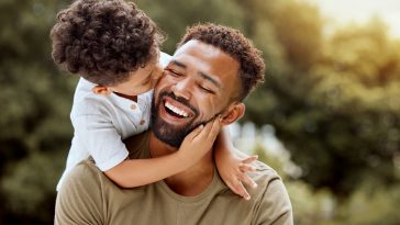 Father, bonding kiss and boy child hug happy in nature with quality time together outdoor. Happiness, laughing and family love of a dad and kid in a park enjoying nature hugging with care and a smile.