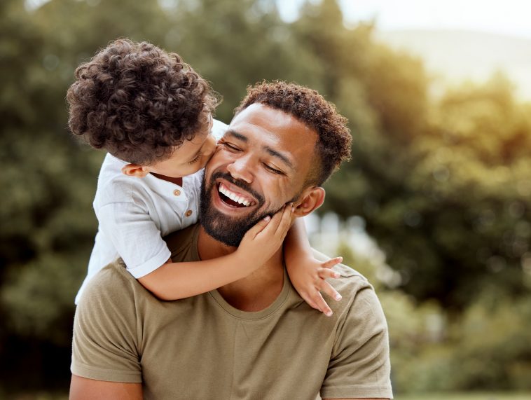 Father, bonding kiss and boy child hug happy in nature with quality time together outdoor. Happiness, laughing and family love of a dad and kid in a park enjoying nature hugging with care and a smile.