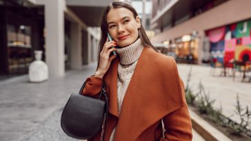 Cute brunette woman in brown coat talking on the phone in the city close up