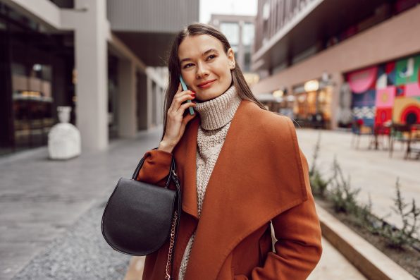 Cute brunette woman in brown coat talking on the phone in the city close up