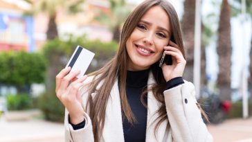 Young pretty woman at outdoors buying with the mobile with a credit card while thinking