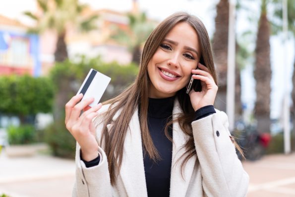 Young pretty woman at outdoors buying with the mobile with a credit card while thinking