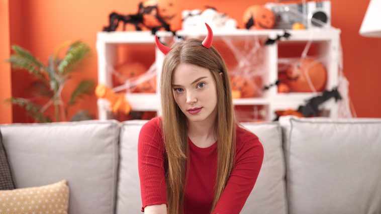 Young blonde woman wearing devil costume sitting on the sofa at home