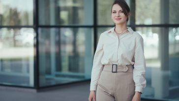 Business portrait of caucasian young woman in office or business style in clothes in beige tones against the backdrop of an office building.