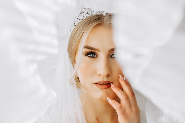 The bride in a white dress, veil poses in beautiful lighting in her room. Morning of the bride. A beautiful tiara