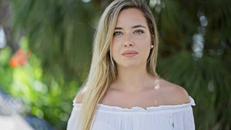 Young blonde woman standing with serious expression at park