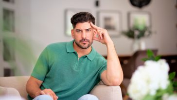 A middle-aged man sitting in his armchair at home. Confident male wearing shirt and jeans and looking thoughtfully.