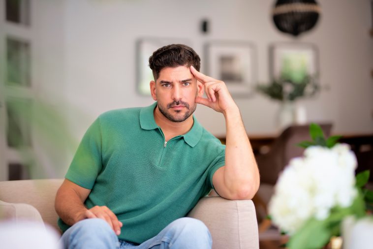 A middle-aged man sitting in his armchair at home. Confident male wearing shirt and jeans and looking thoughtfully.