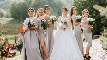 Group portrait of the bride and bridesmaids. A bride in a wedding dress and bridesmaids in silver dresses hold stylish bouquets on their wedding day.