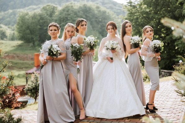 Group portrait of the bride and bridesmaids. A bride in a wedding dress and bridesmaids in silver dresses hold stylish bouquets on their wedding day.