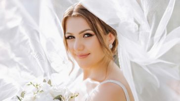 Beautiful bride with wedding flowers bouquet, attractive woman in wedding dress. Happy newlywed woman. Bride with wedding makeup and hairstyle. Smiling bride. Wedding day. Gorgeous bride. Marriage.