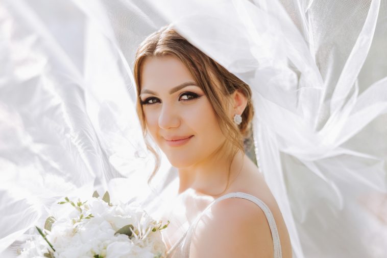 Beautiful bride with wedding flowers bouquet, attractive woman in wedding dress. Happy newlywed woman. Bride with wedding makeup and hairstyle. Smiling bride. Wedding day. Gorgeous bride. Marriage.