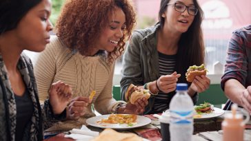 Restaurant, group and friends eating, social gathering and reunion with conversation and happiness. Diversity, women and student on a break, fast food and snack with lunch and smile with discussion.