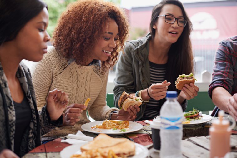 Restaurant, group and friends eating, social gathering and reunion with conversation and happiness. Diversity, women and student on a break, fast food and snack with lunch and smile with discussion.