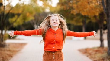 Smiling teenage girl 14-15 year old having fun over autumn leaves background close up. Looking at camera. Fall season.