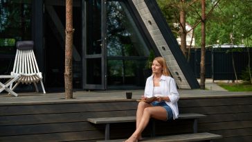 Woman, writing noteson the steps of the A-frame house. Rest, notepad and student with creative ideas, inspiration and planning to do list on journal