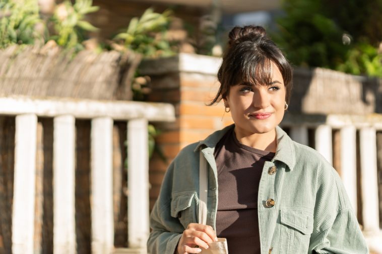 A woman wearing a green jacket and holding a white bag. Enjoying a walk on a sunny day outdoors. Lifestyles concept. Close-up