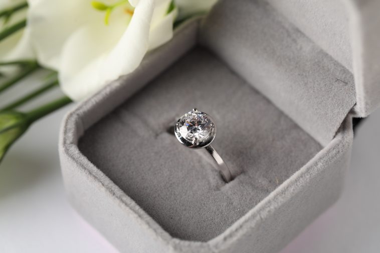 Beautiful ring with gemstone in box and flower on white background, closeup