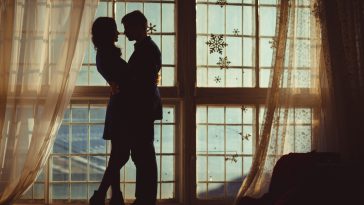 Silhouettes of young couple hugging before panoramic window