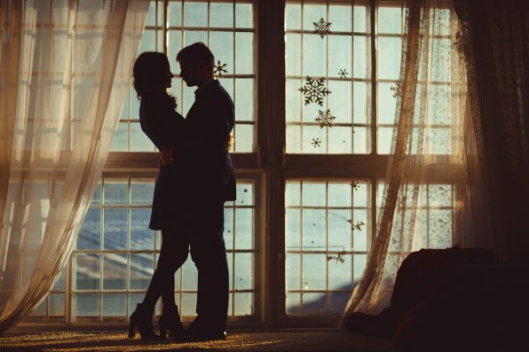 Silhouettes of young couple hugging before panoramic window