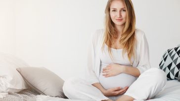 Healthy pregnancy gestation. Portrait of a young pregnant smiling woman sitting in her bedroom resting in the morning holding her tummy waiting for her childbirth.