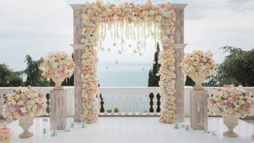 Elegant wedding arch with fresh flowers, vases on background of ocean and blue sky.