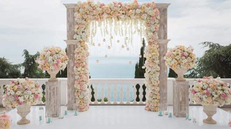 Elegant wedding arch with fresh flowers, vases on background of ocean and blue sky.