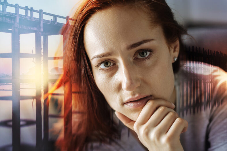 Attentive look. Calm young serious woman sitting at home with her hand touching her chin and thoughtfully looking in front of herself with her eyes wide open