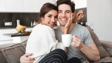 Portrait of a lovely young couple drinking coffee while sitting on a couch and kissing