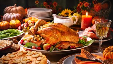 Thanksgiving dinner. Roasted turkey garnished with cranberries on a rustic style table decoraded with pumpkins, vegetables, pie, flowers and candles