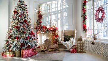 White room interior in red tones with New Year tree decorated, present boxes and artificial fireplace