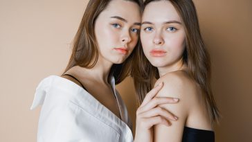 Fashion models two sisters twins beautiful nude girls looking at the camera isolated on beige background