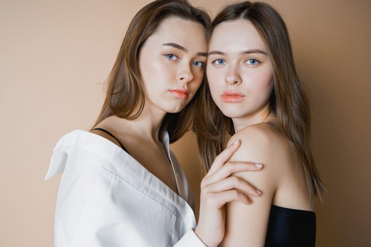 Fashion models two sisters twins beautiful nude girls looking at the camera isolated on beige background