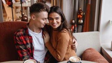 Picture of a cute young happy loving couple sitting in cafe indoors hugging.