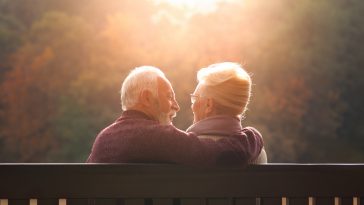 Senior couple sitting on bench in autumn park and looking sunset